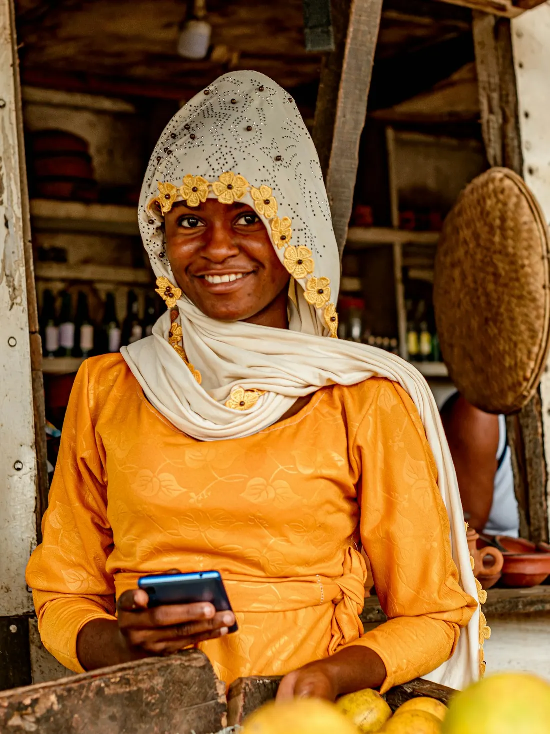 A shopkeeper smiling at her stall with her phone in hand
